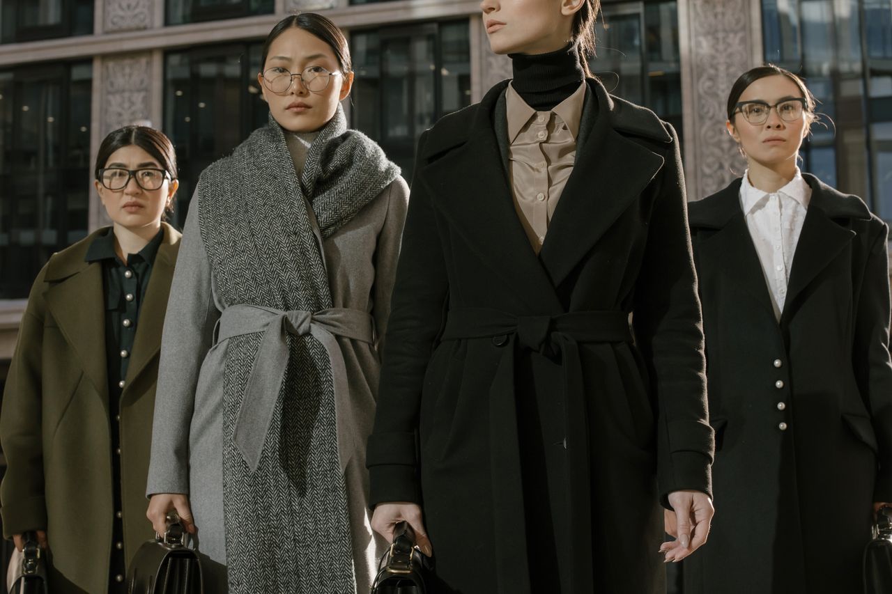 A group of fashionable women in coats standing confidently in an urban environment.